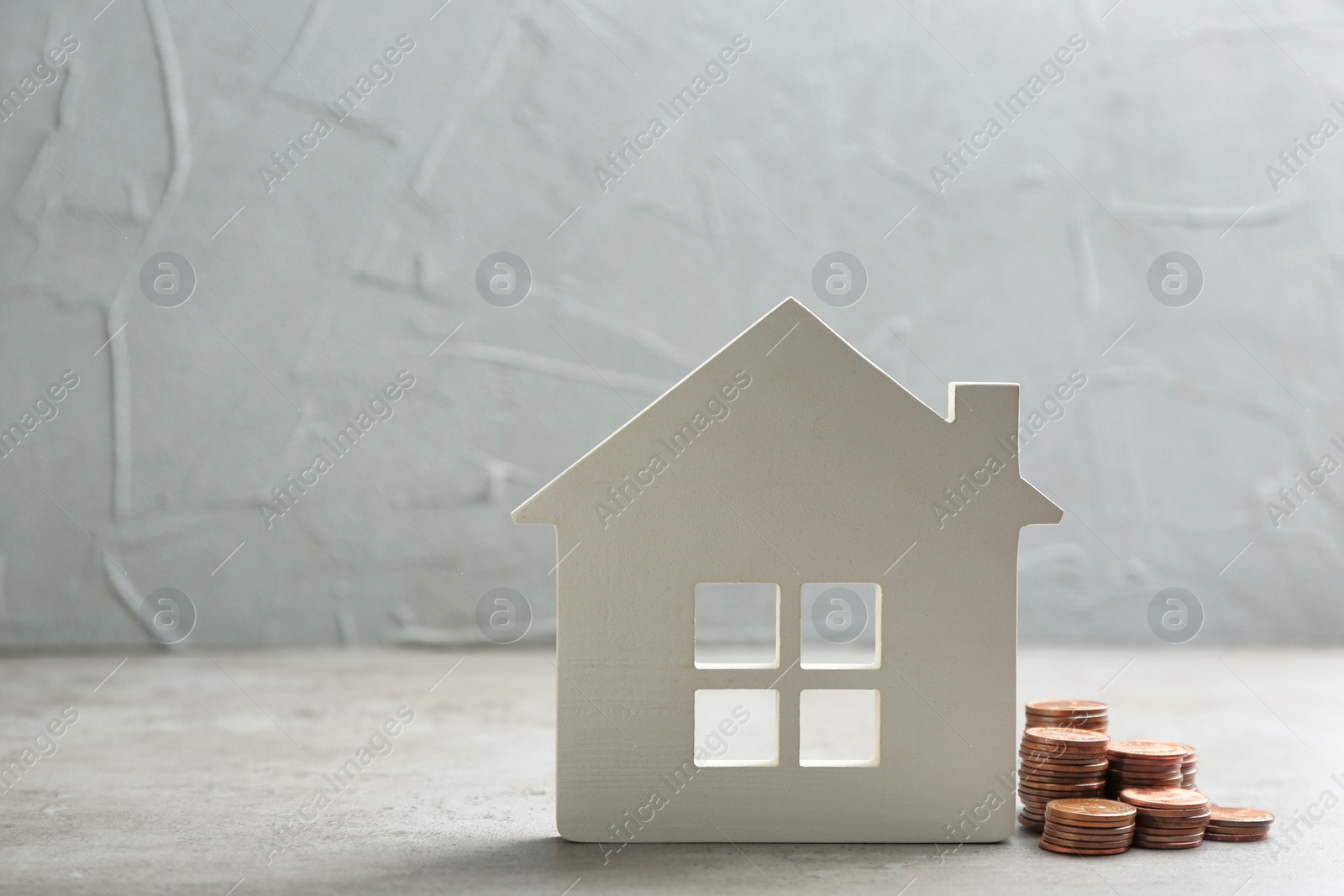 Photo of House figure and coins on table against grey background. Space for text