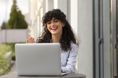 Photo of Happy young woman using modern laptop for video call at table outdoors