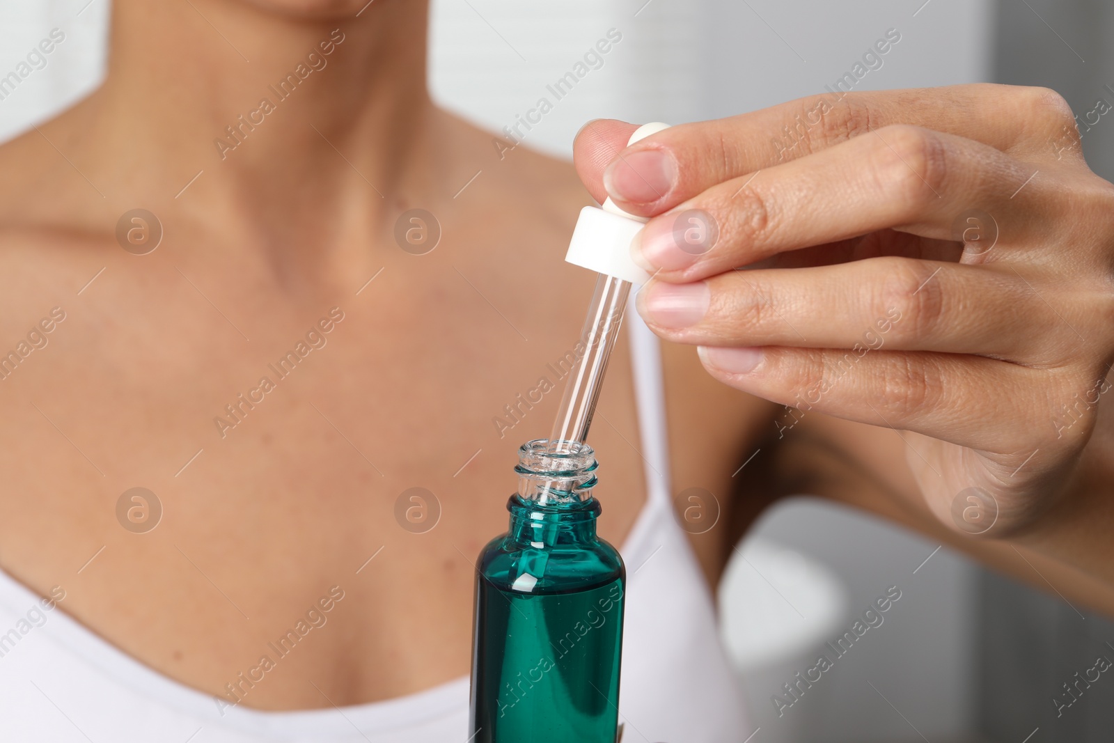 Photo of Woman with bottle of cosmetic serum on blurred background, closeup