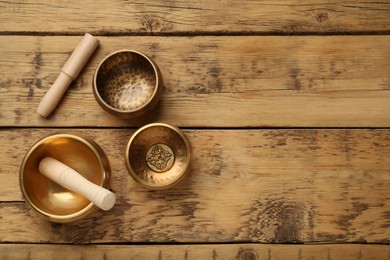 Photo of Golden singing bowls and mallets on wooden table, flat lay. Space for text