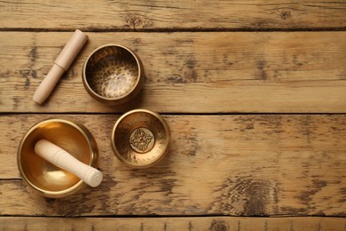 Golden singing bowls and mallets on wooden table, flat lay. Space for text