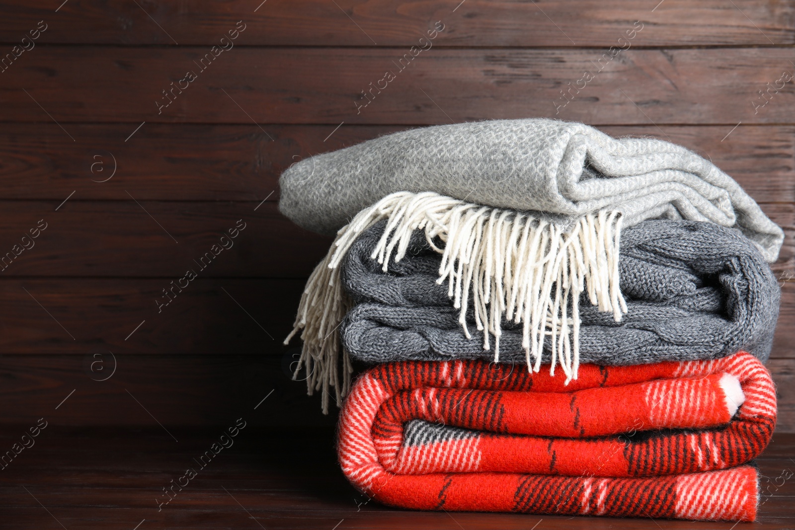 Photo of Stack of soft plaids on brown wooden table, space for text