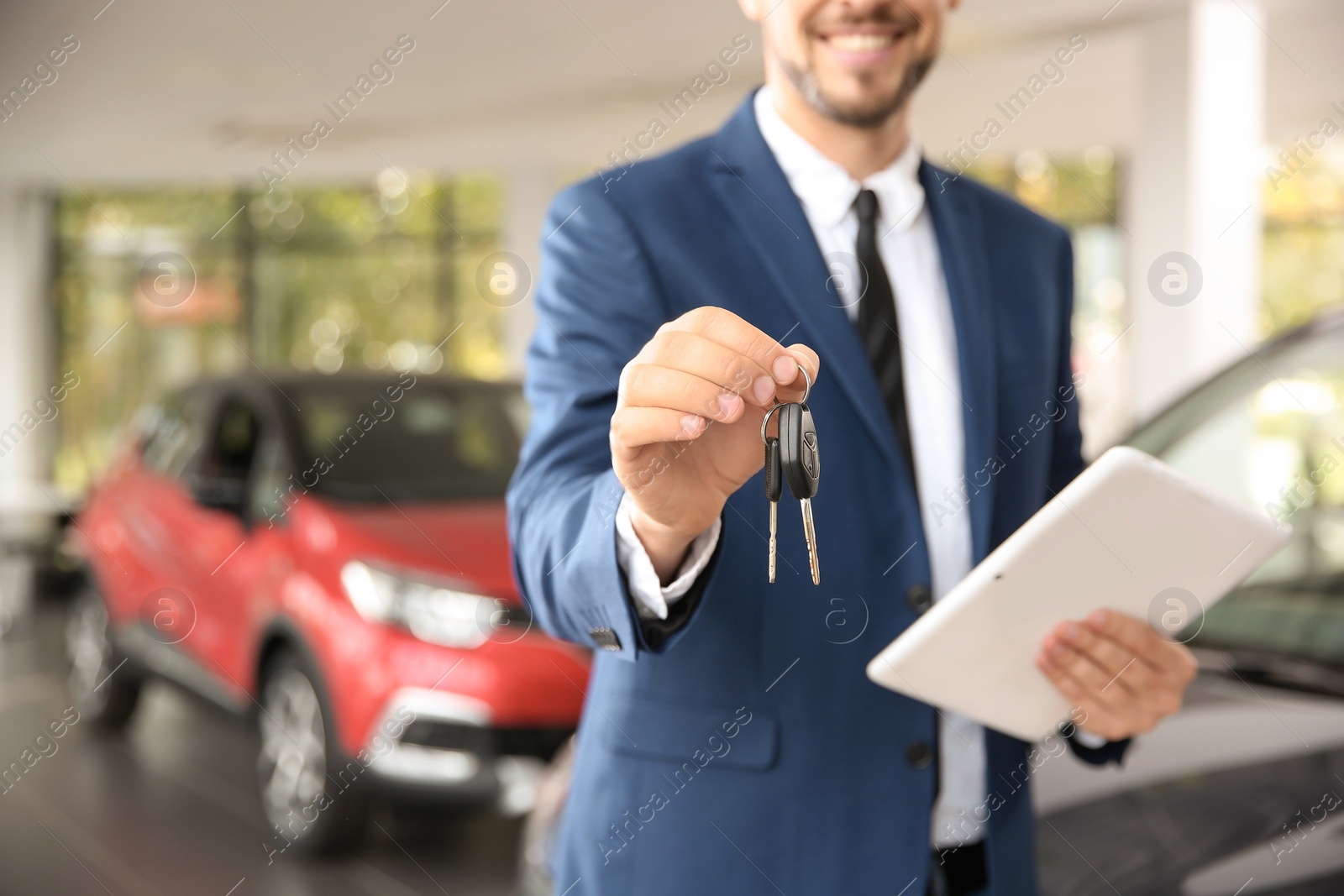 Photo of Salesman with car keys and tablet in auto dealership, closeup