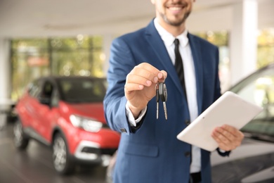 Salesman with car keys and tablet in auto dealership, closeup