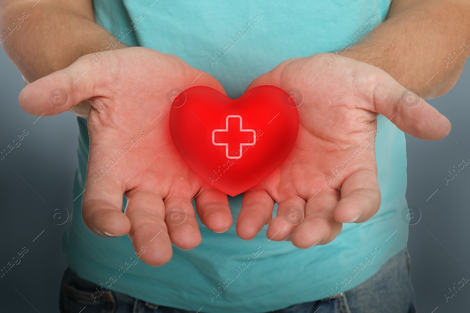 Image of Man holding red heart in hands on color background, closeup. Blood donation concept