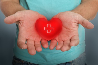 Image of Man holding red heart in hands on color background, closeup. Blood donation concept