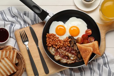 Frying pan with cooked traditional English breakfast on white wooden table, flat lay