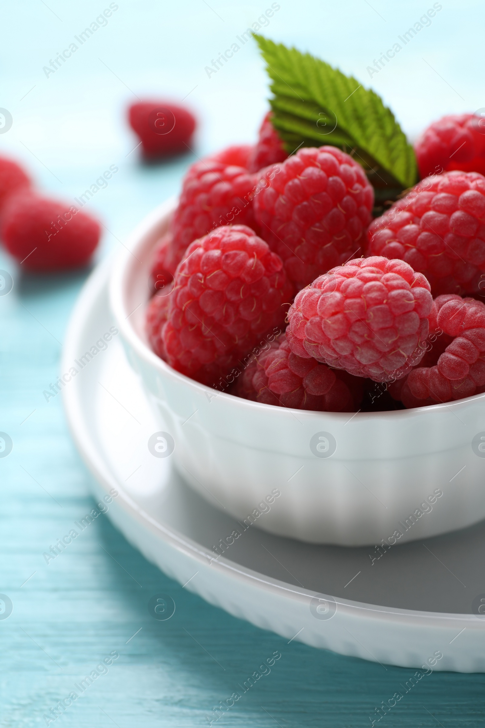 Photo of Delicious ripe raspberries in bowl on light blue wooden table, closeup