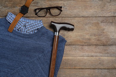Elegant walking cane, sweater, watch and glasses on wooden table, flat lay. Space for text