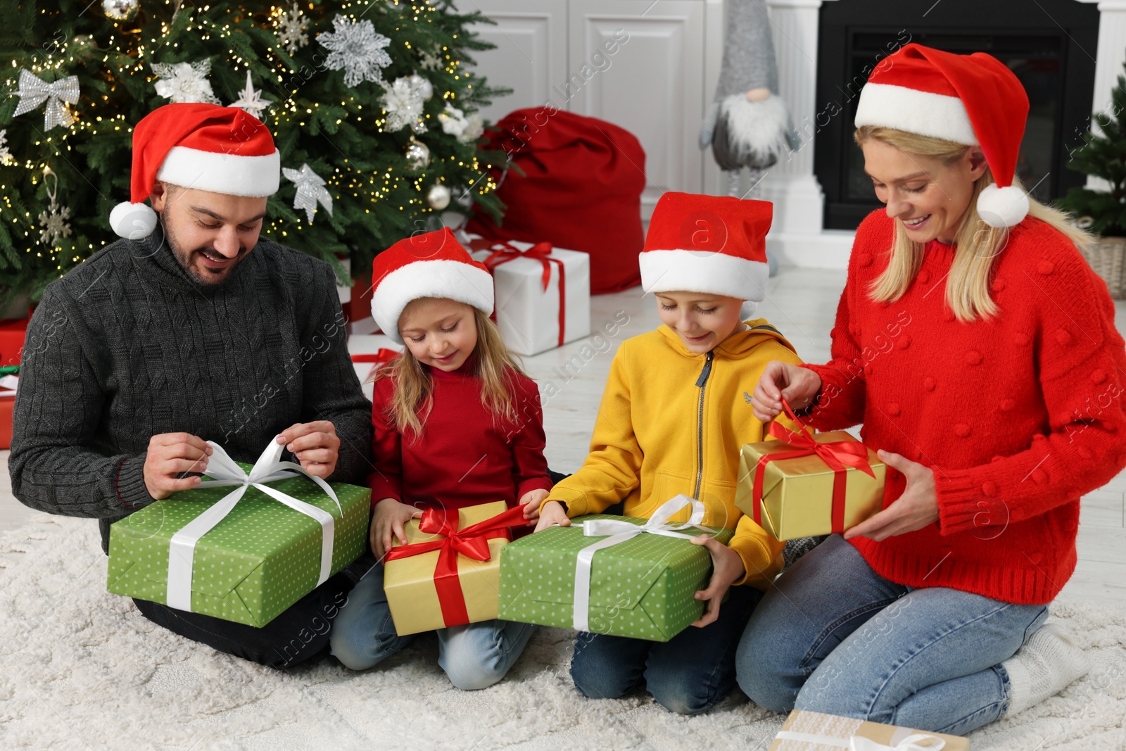 Photo of Happy family in Santa hats opening Christmas gifts at home