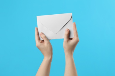 Woman holding white paper envelope on light blue background, closeup