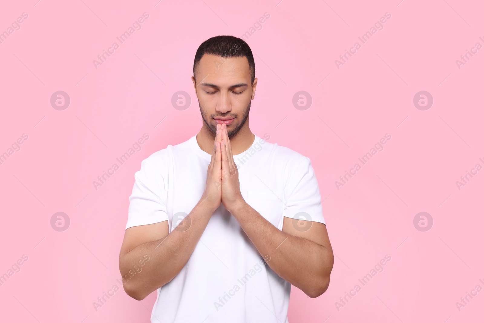 Photo of African American man with clasped hands praying to God on pink background