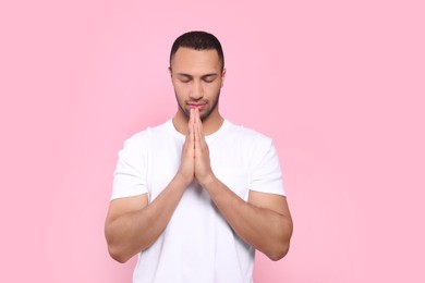 Photo of African American man with clasped hands praying to God on pink background