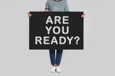 Image of Woman holding poster with text Are You Ready? on light grey background, closeup