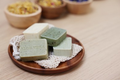 Photo of Tray with soap bars and bowls of dry flowers on light wooden table, space for text. Spa therapy