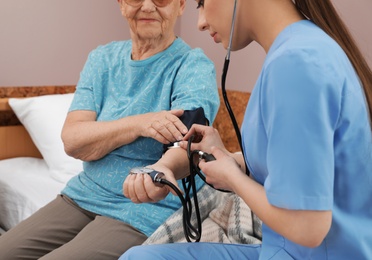 Nurse measuring senior woman's blood pressure in hospital ward, closeup. Medical assisting
