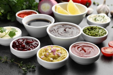 Photo of Different tasty sauces in bowls and ingredients on grey table