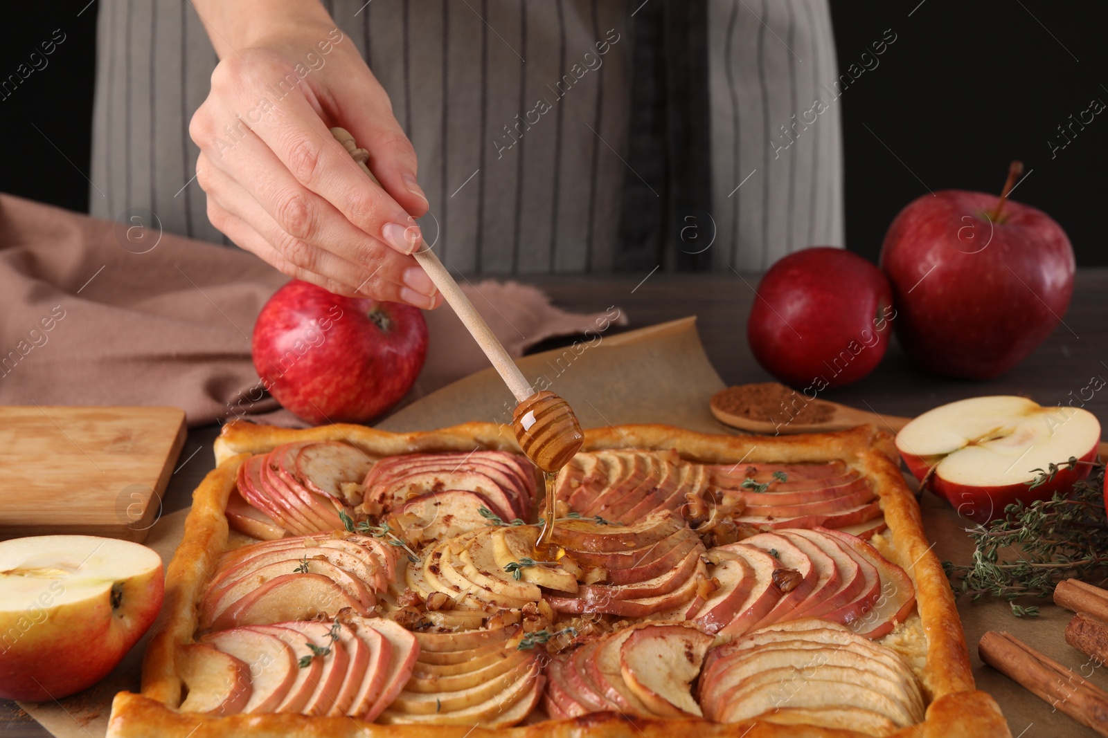 Photo of Woman adding honey to freshly baked apple pie at table, closeup