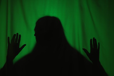 Silhouette of creepy ghost behind dark green cloth