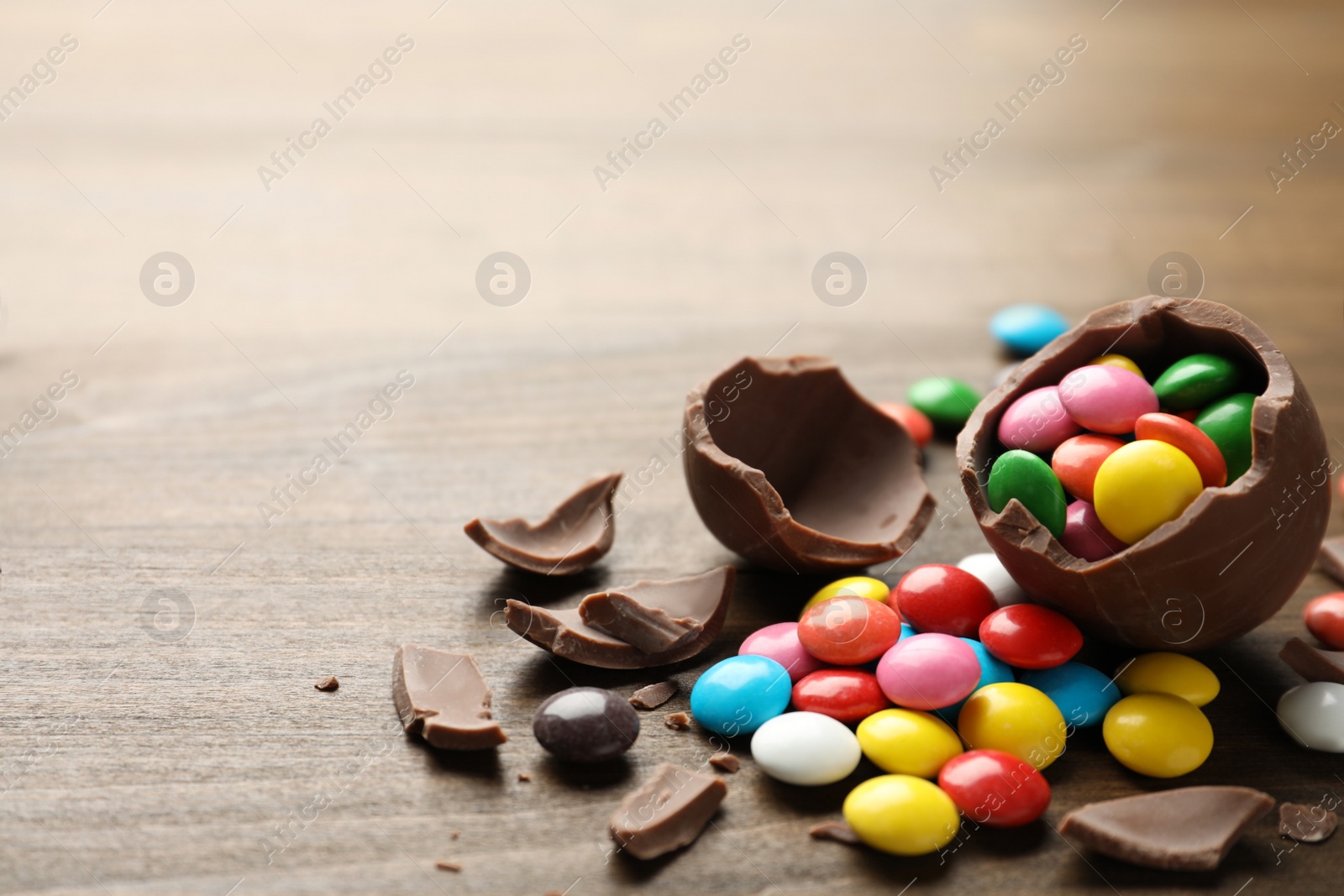 Photo of Broken chocolate egg and colorful candies on wooden table. Space for text