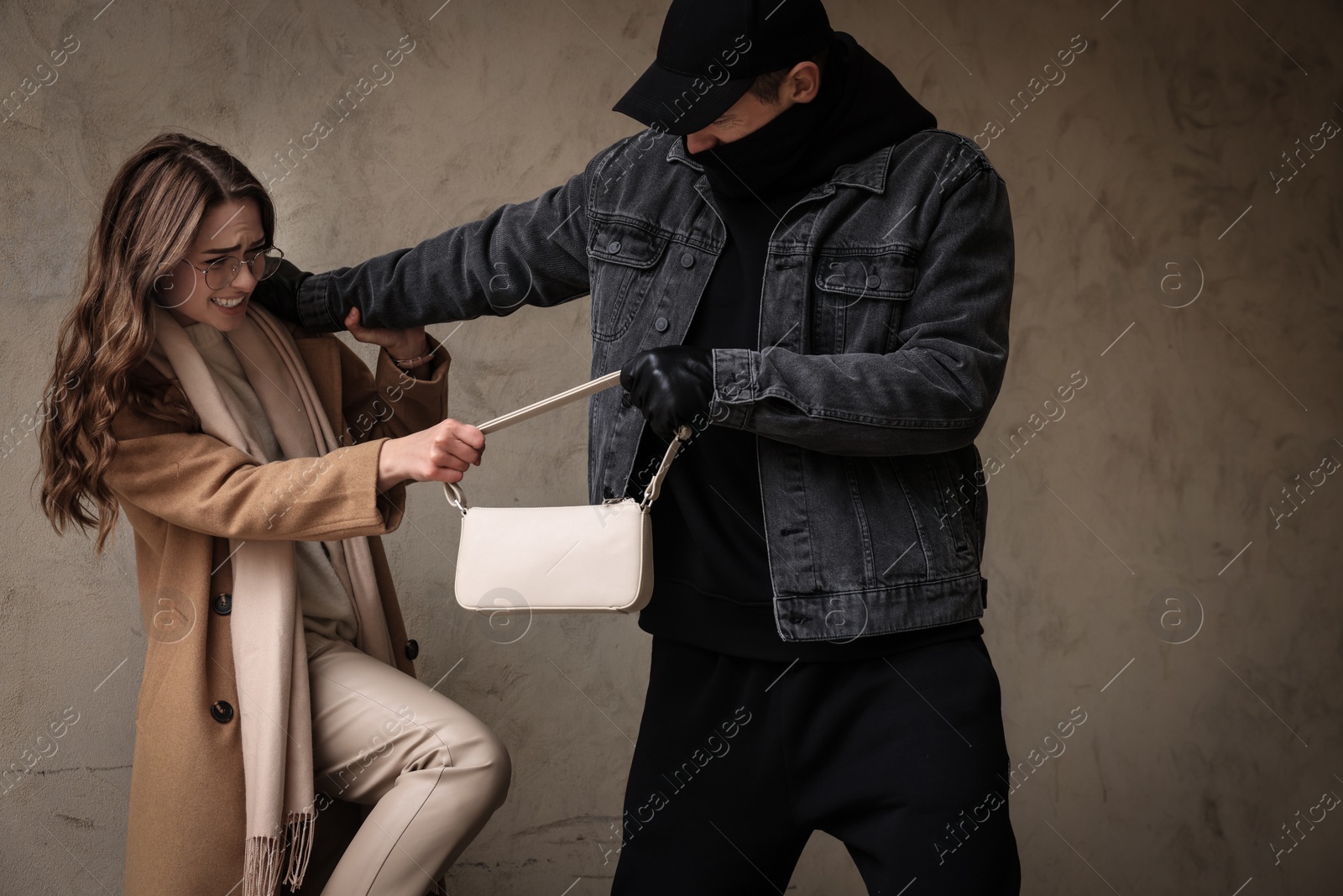 Photo of Woman fighting with thief while he trying to steal her bag near beige wall. Self defense concept