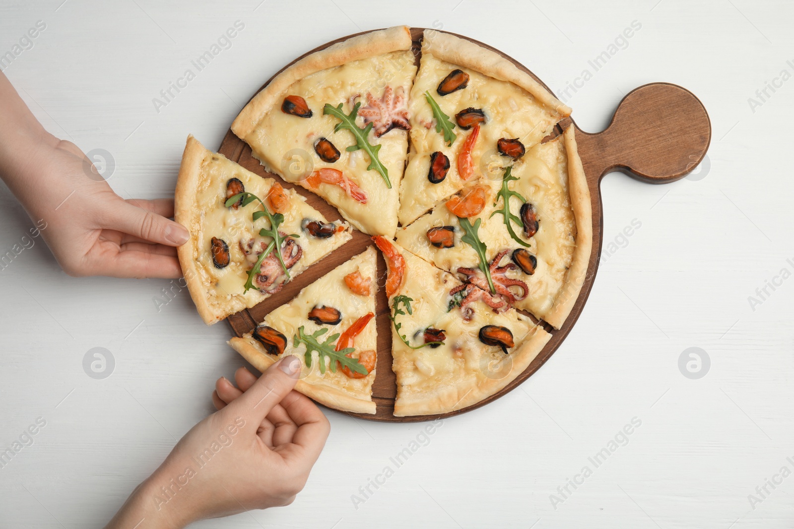 Photo of Women taking pieces of delicious seafood pizza at white wooden table, top view