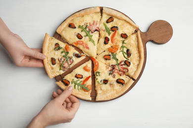 Photo of Women taking pieces of delicious seafood pizza at white wooden table, top view