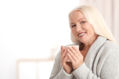 Photo of Portrait of beautiful older woman with cup of tea against blurred background. Space for text