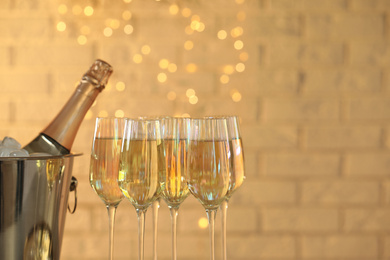 Photo of Glasses of champagne and ice bucket with bottle on blurred background