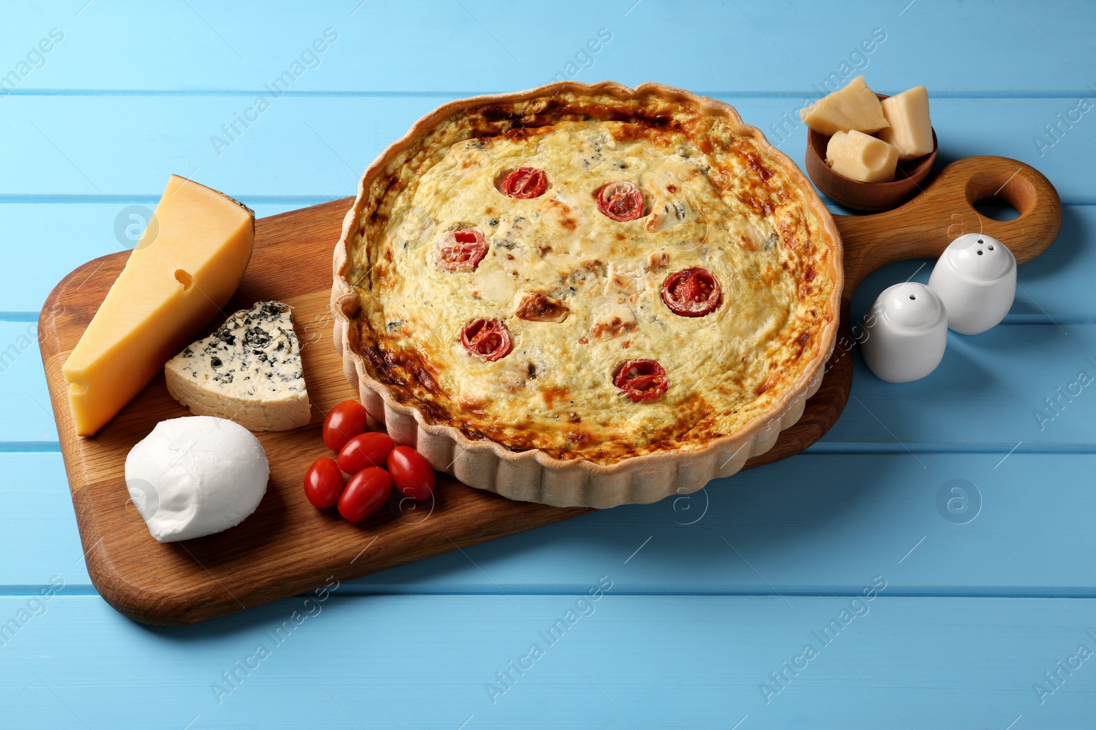 Photo of Delicious homemade cheese quiche and ingredients on light blue wooden table