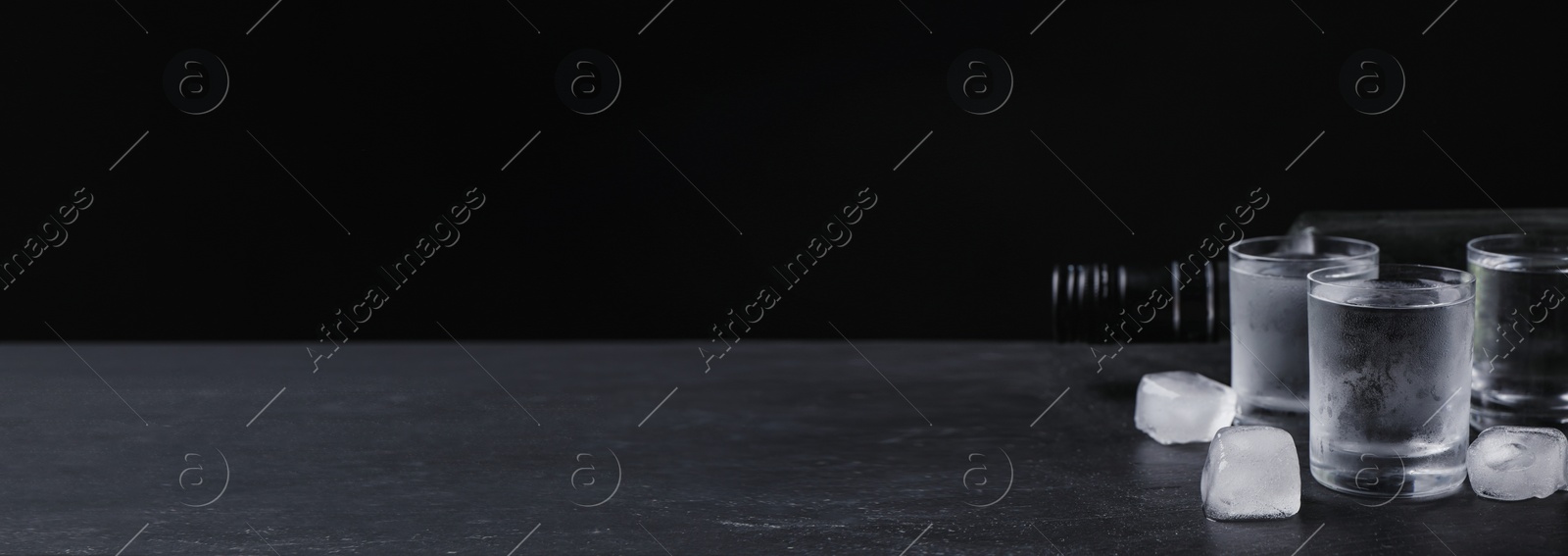 Image of Bottle of vodka and shot glasses with ice on table against black background, space for text. Banner design