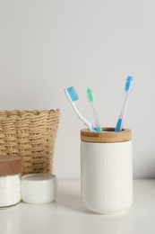Photo of Plastic toothbrushes in holder and cosmetic products on white countertop