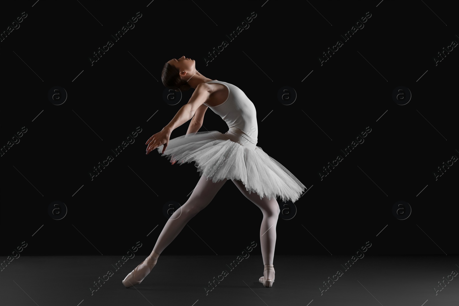 Photo of Young ballerina practicing dance moves on black background