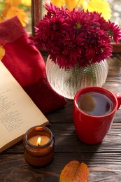 Photo of Beautiful chrysanthemum flowers, candle, cup of tea and book on wooden table indoors. Autumn still life
