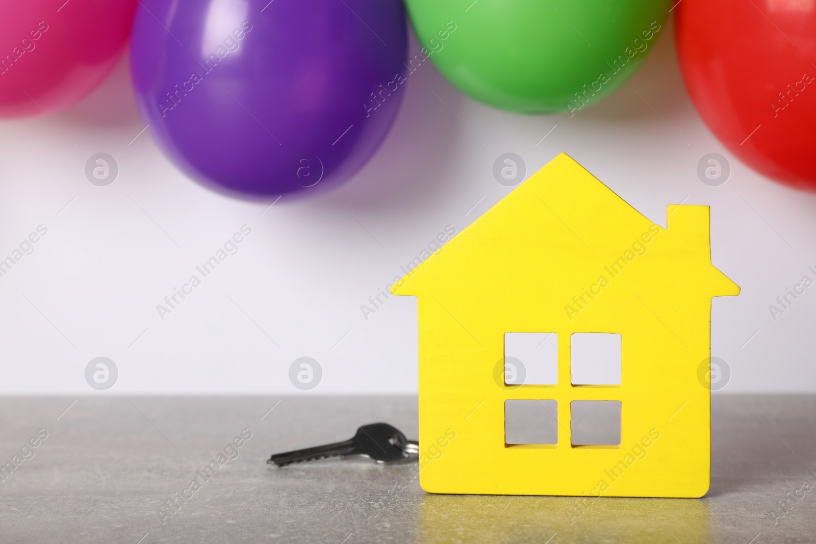 Photo of Yellow house model with key and balloons on grey table, space for text. Housewarming party