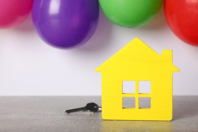 Yellow house model with key and balloons on grey table, space for text. Housewarming party