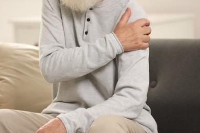 Photo of Senior man suffering from pain in arm indoors, closeup. Rheumatism symptom