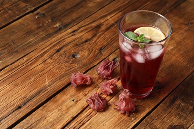 Photo of Glass of delicious iced hibiscus tea and dry flowers on wooden table, space for text