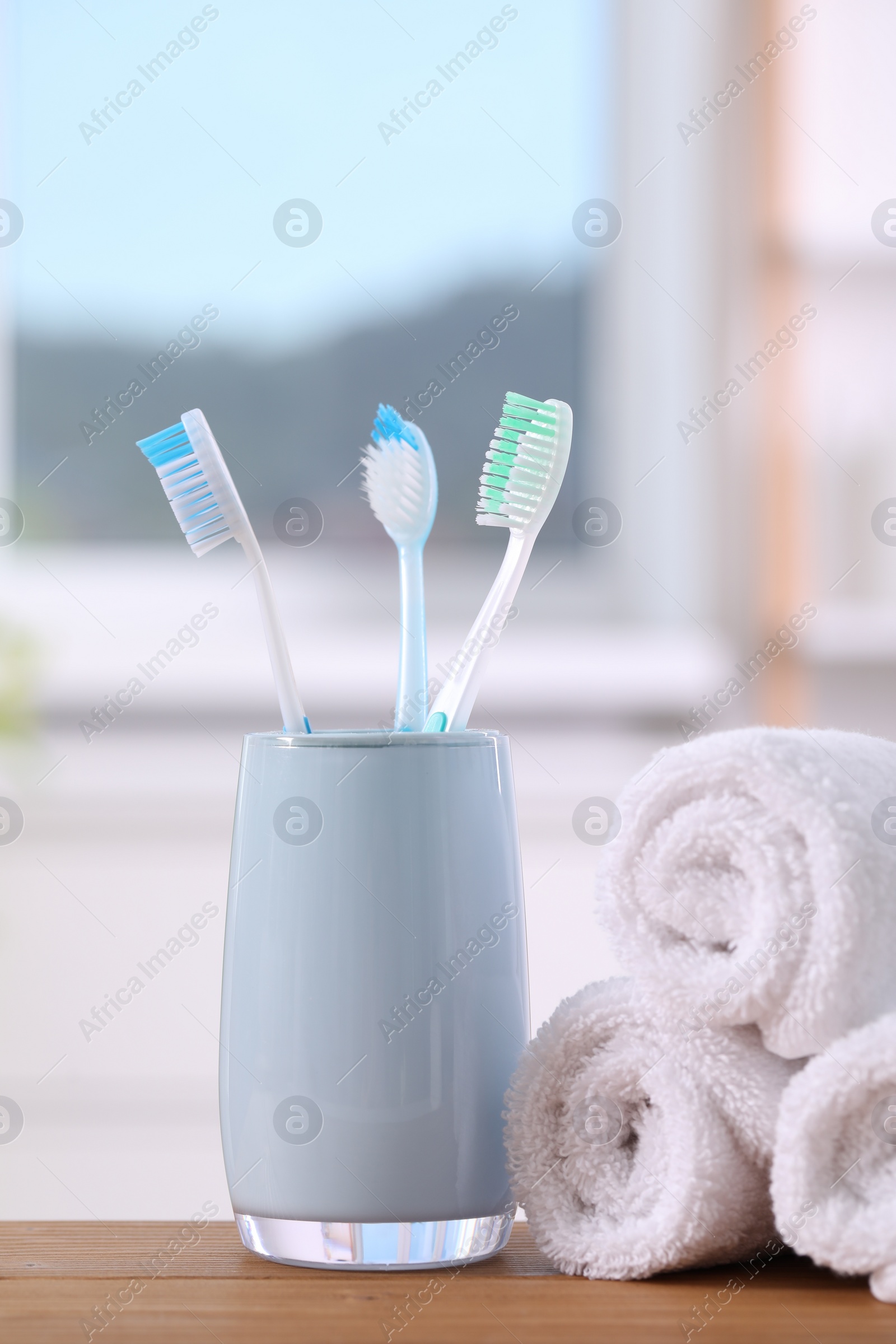 Photo of Plastic toothbrushes in holder and towels on wooden table indoors