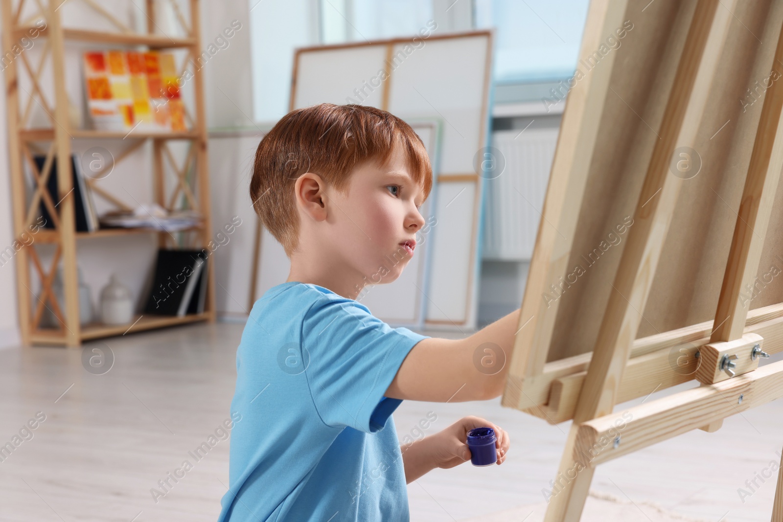 Photo of Little boy painting in studio. Using easel to hold canvas