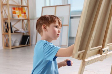 Little boy painting in studio. Using easel to hold canvas