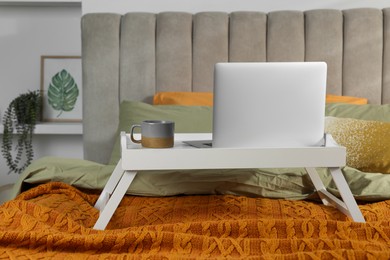 White tray with modern laptop and cup of aromatic drink on bed indoors
