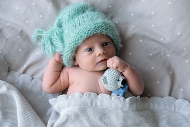 Photo of Cute newborn baby in warm hat with toy lying on bed, top view