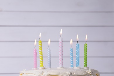 Delicious cake with cream and burning candles near white wall, closeup