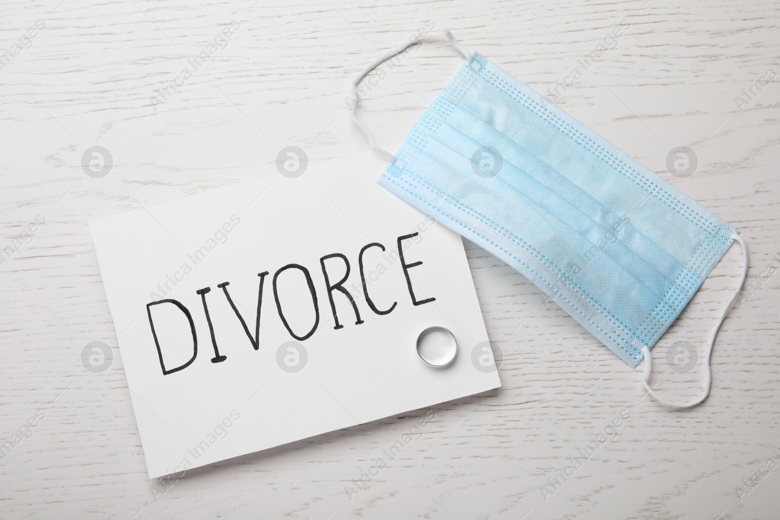 Photo of Flat lay composition with protective mask and wedding ring on white wooden table. Divorce during coronavirus quarantine