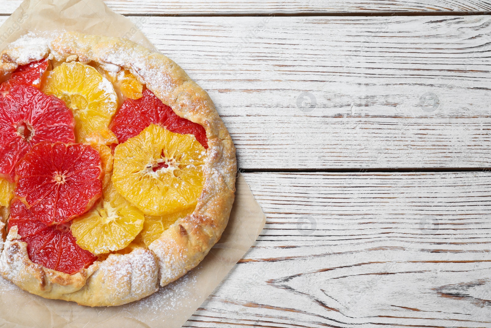 Photo of Delicious galette with citrus fruits on white wooden table, top view. Space for text