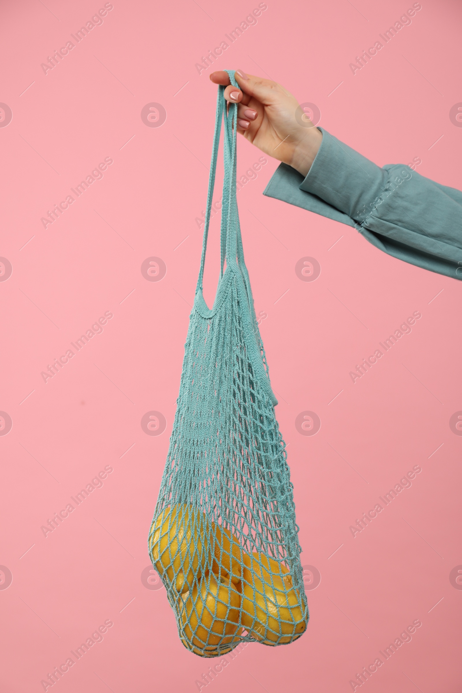 Photo of Woman with string bag of fresh lemons on pink background, closeup