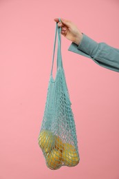 Woman with string bag of fresh lemons on pink background, closeup