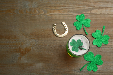 Photo of Green beer, horseshoe and clover leaves on wooden table, flat lay with space for text. St. Patrick's Day celebration