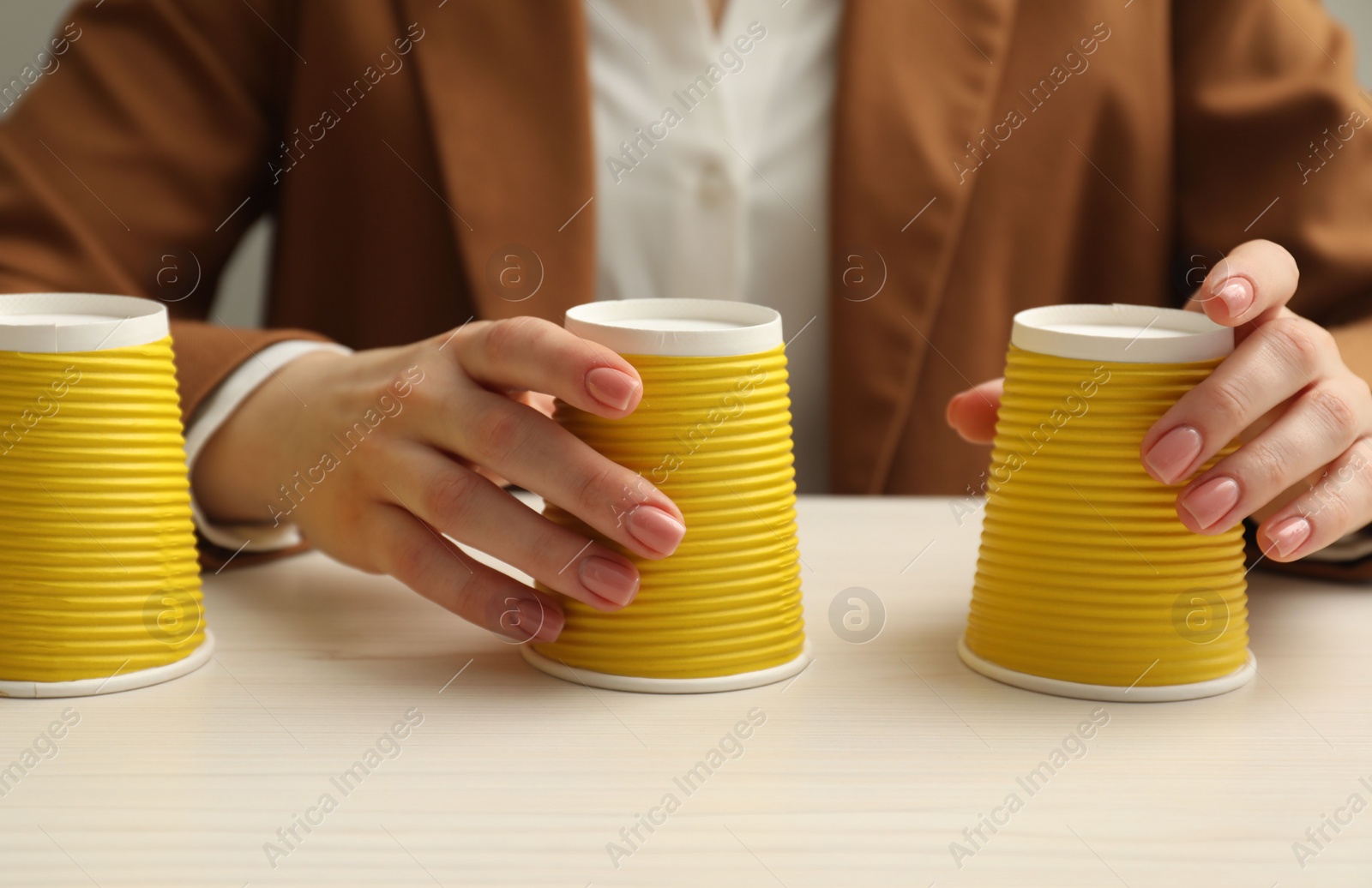 Photo of Woman playing shell game with yellow cups at white wooden table, closeup